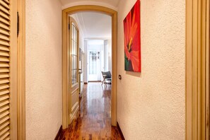 A hallway with a wooden floor, a door with a glass panel, and a painting on the wall. - Capitan Romeo Apartment (Arenzano)