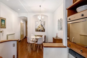 A dining area with a round table and chairs, a chandelier, and a painting on the wall. - Capitan Romeo Apartment (Arenzano)