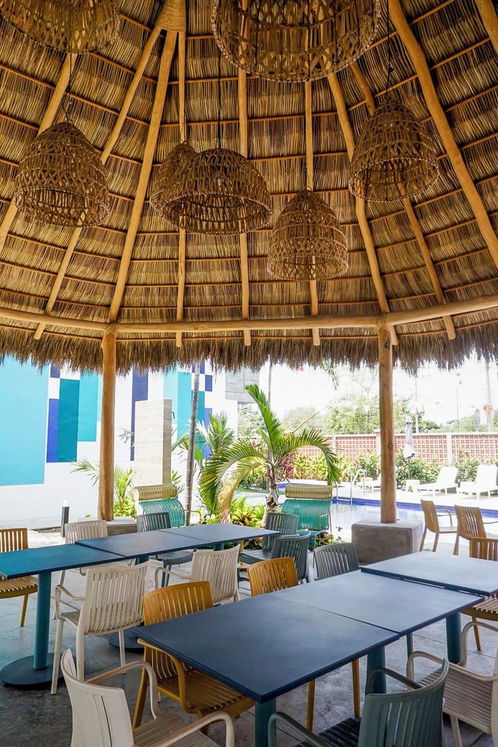 An outdoor seating area with tables and chairs, a thatched roof, and hanging wicker lamps.