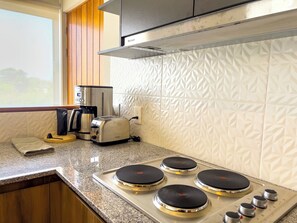 Uma cozinha com fogão a gás de quatro bocas, cafeteira, torradeira e janela com vista para árvores.
