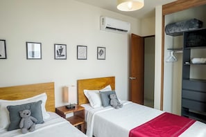 Quarto de hotel com duas camas, um guarda-roupa e uma mesa de cabeceira com abajur.