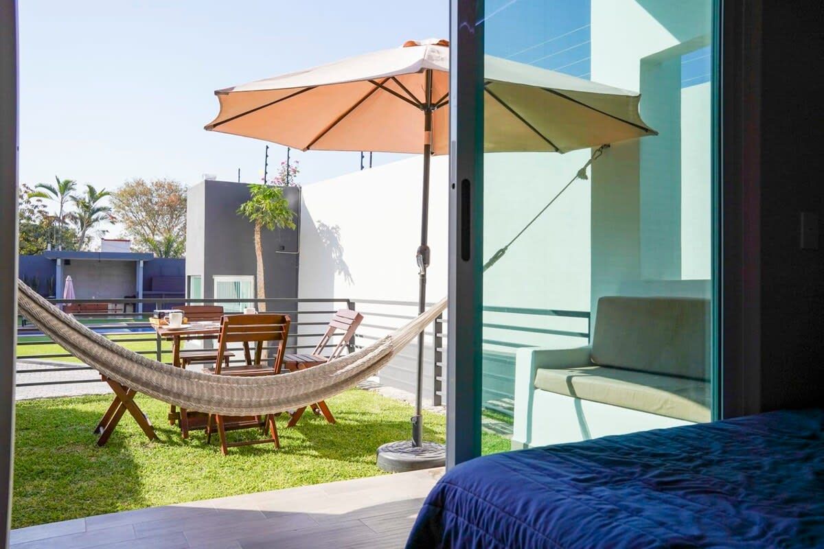 A room with a bed, a hammock, a table with chairs, and an umbrella.