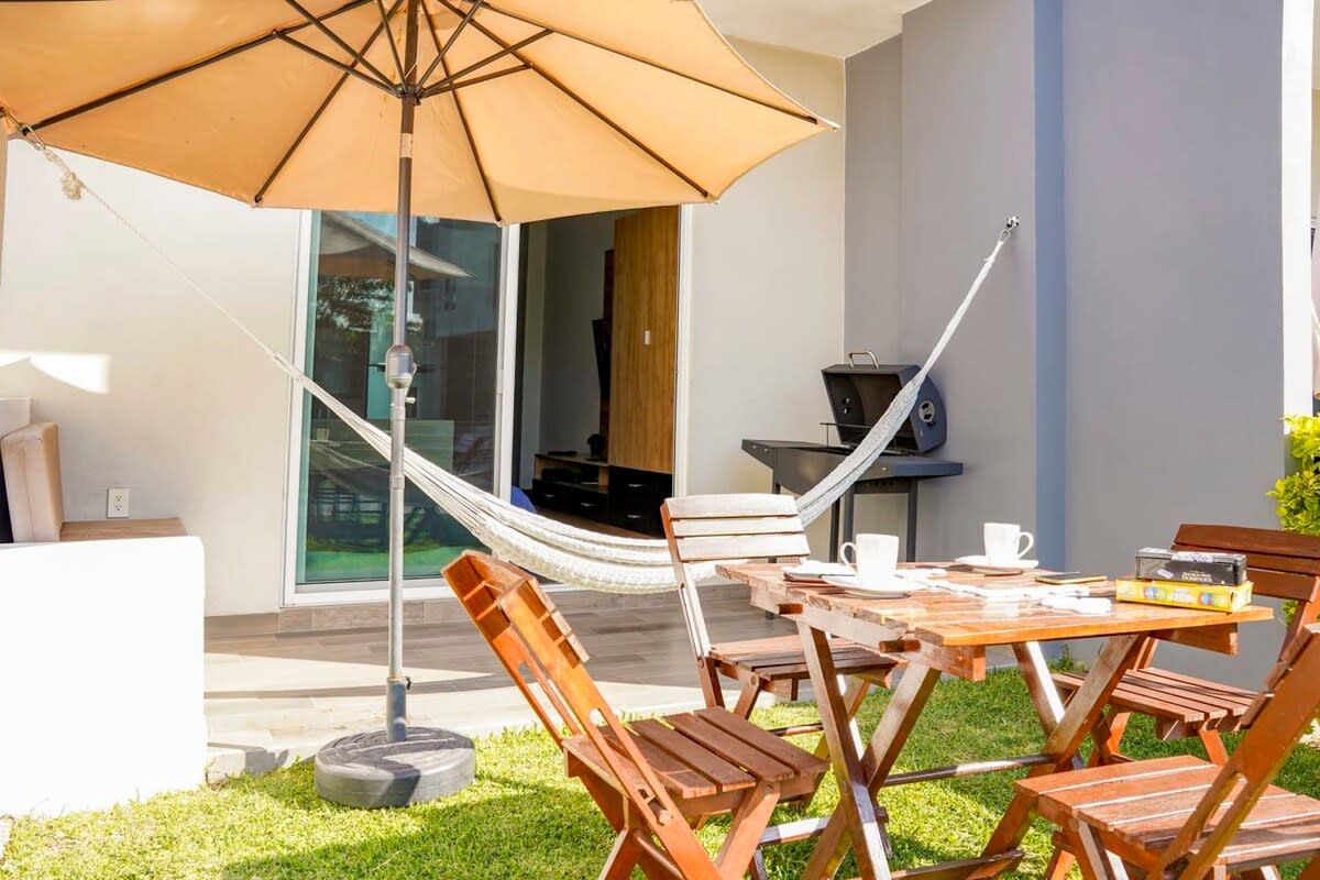 Un pati exterior amb taula i caires de fusta, una cadira sisenya i una barbacoa.