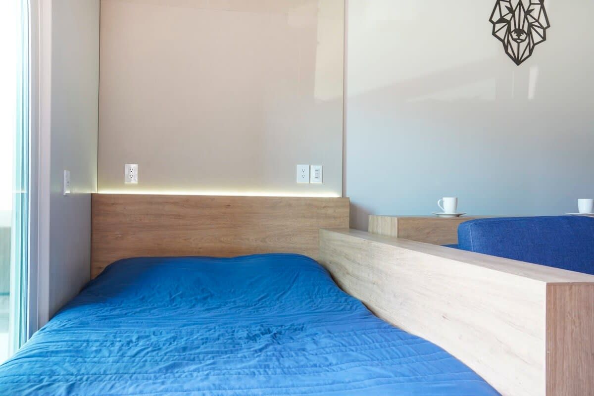 A room with a bed, a wooden headboard, a wall-mounted light, and a small table with a cup.