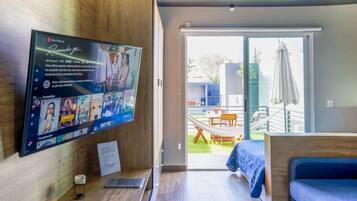 Moderni huone, jossa on televisio, jolta näkyy elokuva, sänky, työpöytä lampun kanssa ja näkymä ulos.