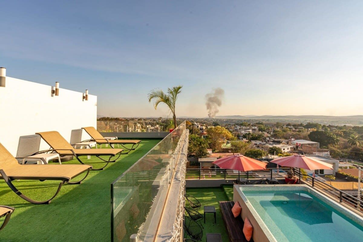 Terraza en la azotea con sillones de descanso, piscina y vistas a un paisaje urbano.