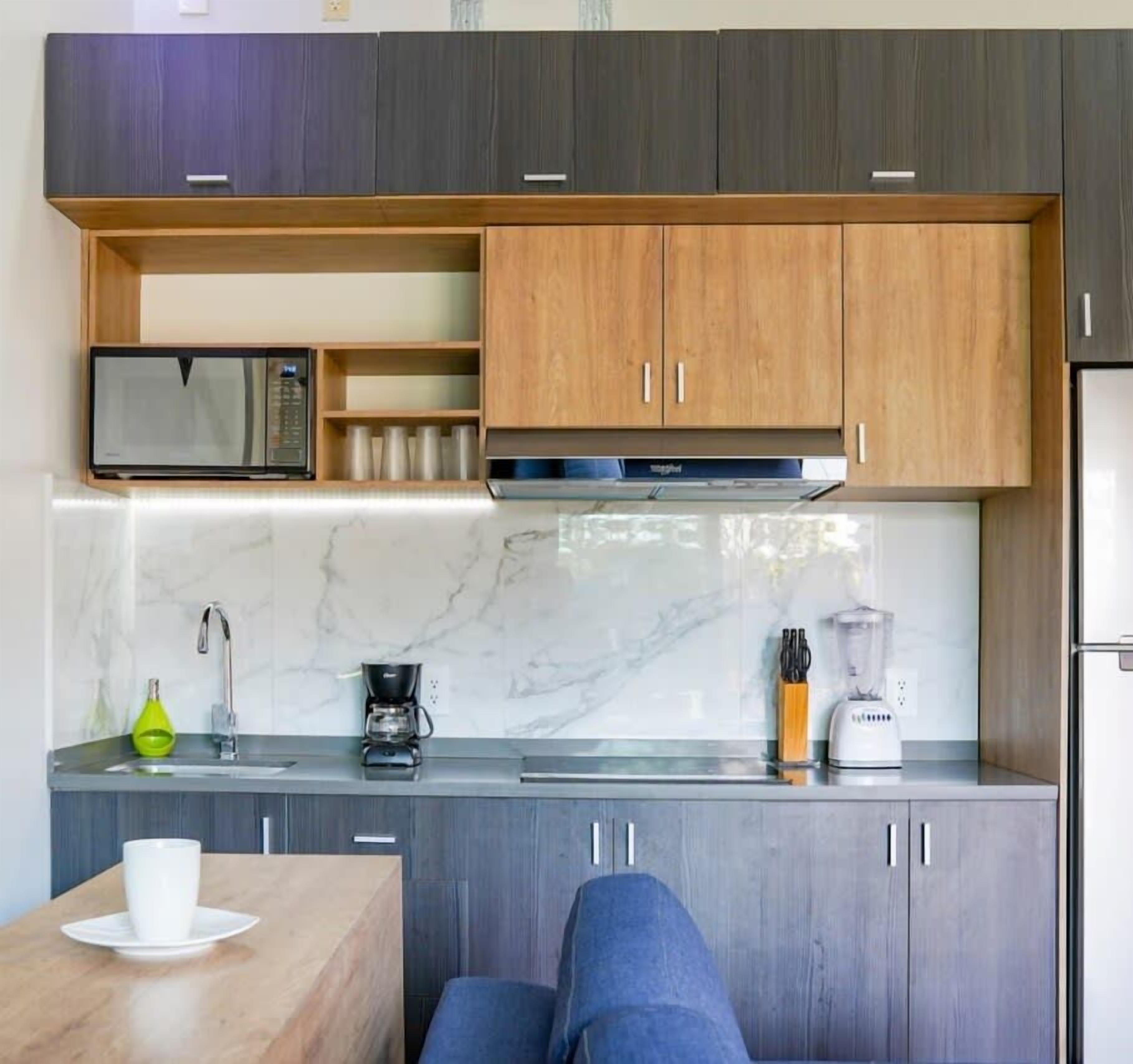 Una cocina moderna con microondas, cafetera y licuadora en la encimera, y una zona de estar con mesa y sillas.