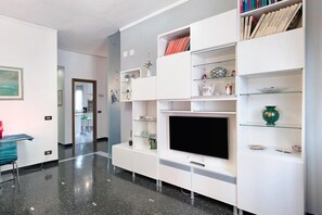 A modern living room with a flat-screen TV, white shelving units, and a glass coffee table. - Casa Andrea - Two Bedroom Apartment, Sleeps 4 (Arenzano)