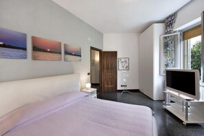 Et hotelværelse med seng, fjernsyn, skrivebord og et vindue med gardiner.