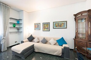 Ein Wohnzimmer mit Ecksofa, einer Schranke mit Glastüren und Wandregalen mit Dekorationselementen.