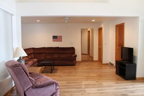 A living room with a brown sofa, a small table, a purple armchair, a television on a stand, and an American flag on the wall. - Lake House with HUGE Beach Front (Grand Junction)