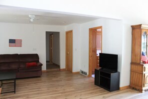 A living room with a wooden floor, a brown sofa, a television, and a wooden cabinet. - Lake House with HUGE Beach Front (Grand Junction)