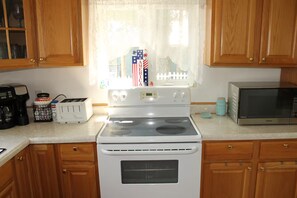 A kitchen with wooden cabinets, a white stove, a toaster, a microwave, and a window with a view of a cityscape. - Lake House with HUGE Beach Front (Grand Junction)