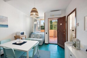 Un espacio habitable compacto con zona de comedor, sofá, televisor y puerta corredera a un área exterior.