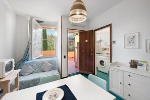 Un espacio habitable compacto con una mesa de comedor, un sofá con cojines estampados, una lavadora y una kitchenette.
