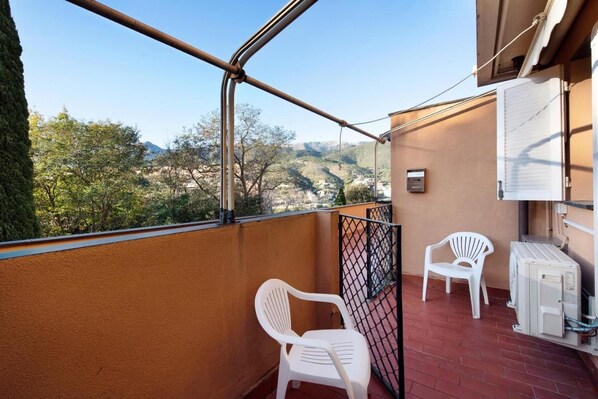 Ein Balkon mit Blick auf eine gebirgige Landschaft, ein weißer Plastikstuhl und ein weißer Plastiktisch.