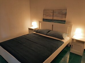 Una cama individual con una colcha oscura, dos almohadas, un cabecero y dos lámparas de noche.