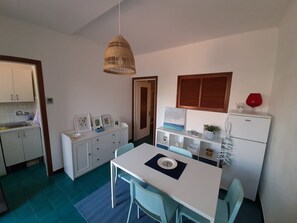 Una cocina compacta con armarios blancos, un comedor con mesa y sillas, y una lámpara colgante.