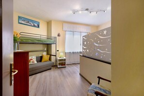 Ein Zimmer mit einem Etagenbett, einer Schlafcouch, einem kleinen Tisch mit Lampe und einer dekorativen Wandverkleidung.