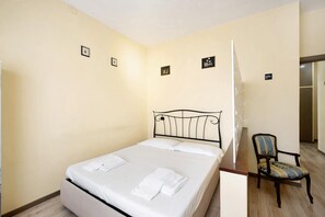 Ein Einzelbett mit weißen Bettwäsche und einem Metall-Kopfstück in einem Zimmer mit cremefarbenen Wänden und Holzboden.