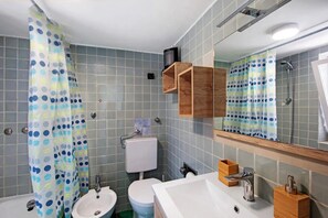 Casa de banho com chuveiro, duas pias, sanita e espelho.
