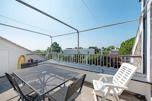 Ein Balkon mit Tisch und Stühlen, ein gelber Gartenschlauch und Blick auf Gebäude und Bäume.