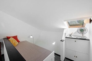 Een kleine, compacte kamer met een bed, een bureau, een stoel, een lamp en een raam.