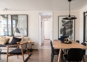 A modern living space with a sofa, a dining table, and chairs. There are abstract paintings on the walls and a large black and white photograph. - Edificio Sucre Ñuñoa by Domus Travels (Ñuñoa)