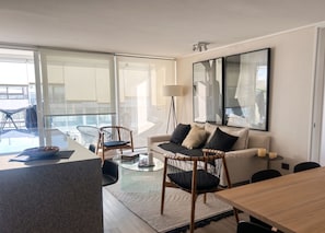 A modern living room with a sofa, chairs, a dining table, and a large window. - Edificio Sucre Ñuñoa by Domus Travels (Ñuñoa)