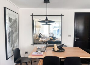 Ein moderner Essbereich mit einem Holztisch, schwarzen Stühlen, einer Pendelleuchte und einem großen gerahmten Bild an der Wand.