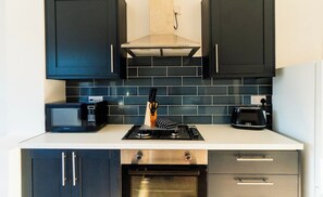 A modern kitchen with dark cabinets, a microwave, a gas stove, and an oven. - Cosy & Stylish Home in St Helens (Saint Helens)