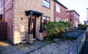 A residential brick house with a front door, a small porch, and a garden with gravel and plants. - Cosy & Stylish Home in St Helens (Saint Helens)