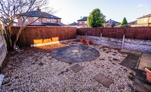 A backyard with a circular stone feature, a wooden fence, and a gravel surface. - Cosy & Stylish Home in St Helens (Saint Helens)