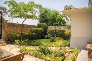 A garden with a stone wall, a variety of plants, and a wooden bench. - Single Room with Private Bathroom (Sheikh Zayed City)