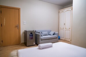 A hotel room with a bed, a grey sofa, a wooden door, and a wardrobe. - Single Room with Private Bathroom (Sheikh Zayed City)