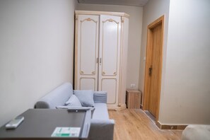 A room with a grey sofa, a small wooden side table, and a wardrobe with two doors. - Single Room with Private Bathroom (Sheikh Zayed City)