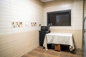 A small, compact room with a tiled floor, a table with a tablecloth, a black television, and a window with blinds. - Single Room with Private Bathroom (Sheikh Zayed City)