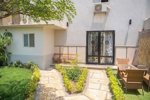 A courtyard with a stone pathway, a wooden bench, a wicker chair, and a gate with decorative metalwork.