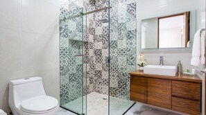 Une salle de bain dotée d’une douche à parois de verre, de toilettes blanches, d’un meuble-lavabo en bois avec un évier et d’un miroir au-dessus du meuble-lavabo.