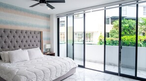 Une chambre moderne avec un grand lit, un ventilateur de plafond et une vue sur un balcon agrémenté de plantes.