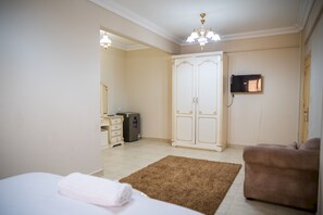 A hotel room with a bed, a brown rug, a wardrobe, a dresser, a television mounted on the wall, and a ceiling light fixture.