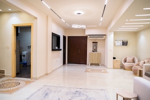 A modern interior with a hallway leading to a room, a wooden door, an air conditioning unit, and a seating area with two chairs. - Double Room with Private Bathroom (Sheikh Zayed City)