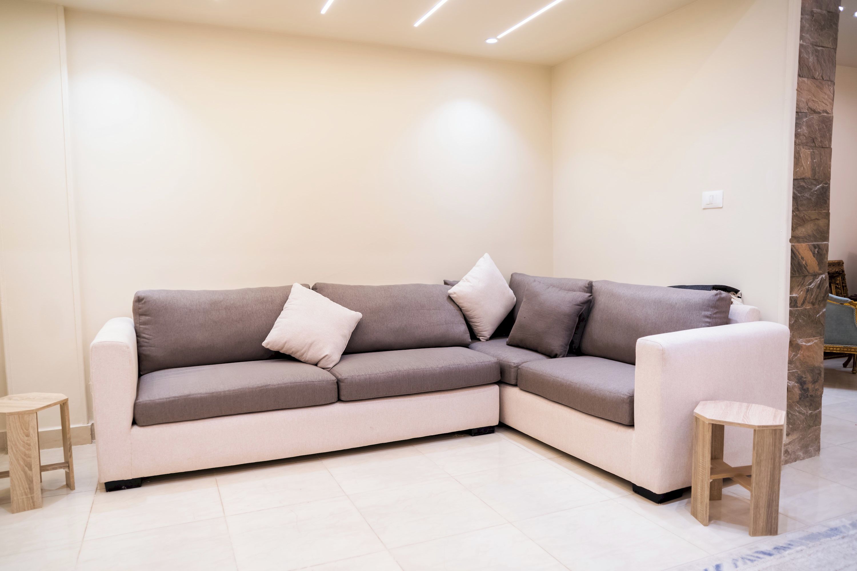 Una sala moderna con un sofá modular, dos taburetes de madera y una pared decorativa de piedra.