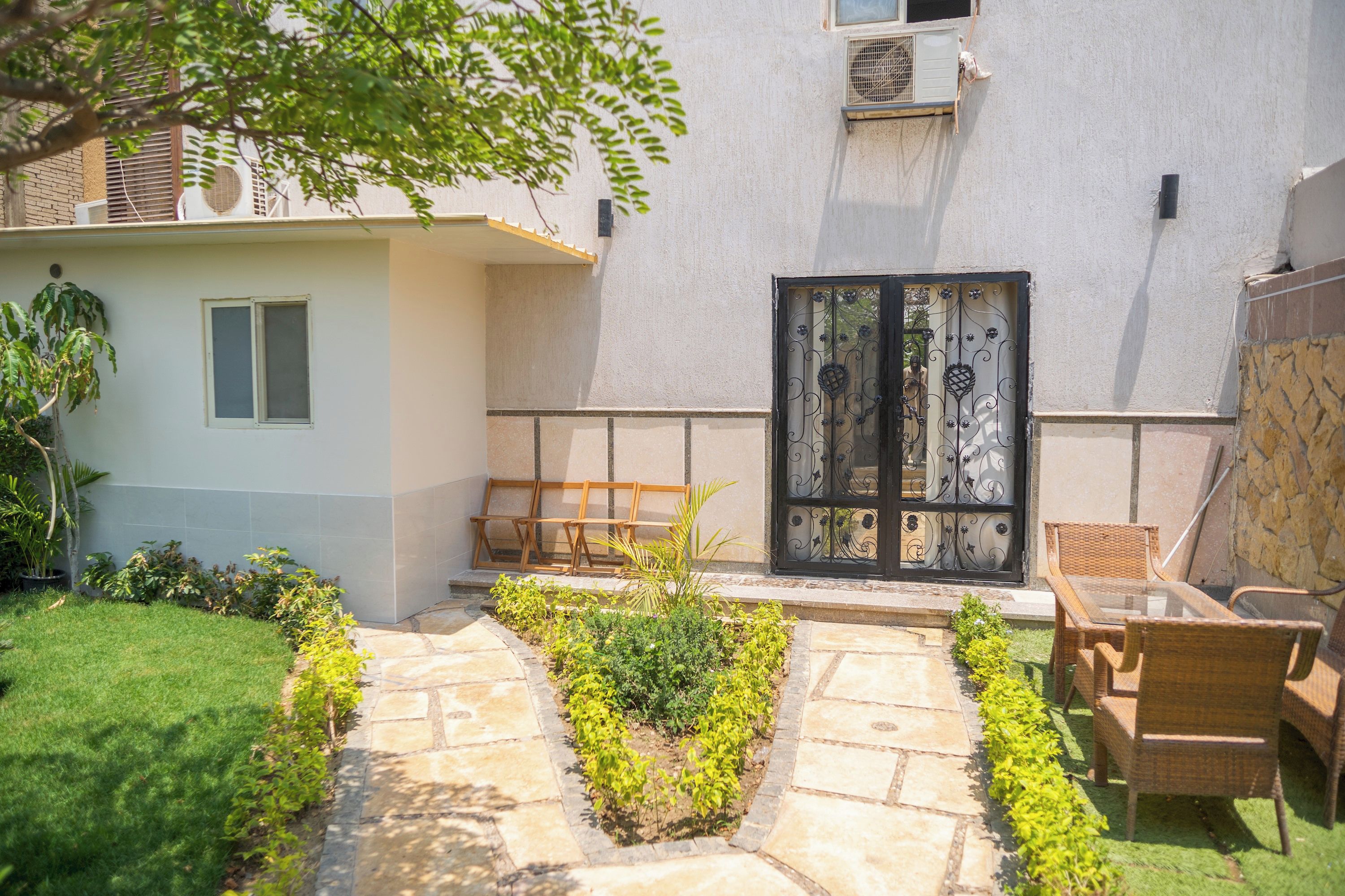 Un patio con un camino de piedra, un banco de madera, una silla de mimbre y una puerta con detalles de metal ornamentado.