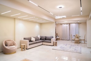 A modern living room with a sectional sofa, a round armchair, a dining table with chairs, and a patterned rug. - Deluxe Twin Room with Panoramic View (Sheikh Zayed City)
