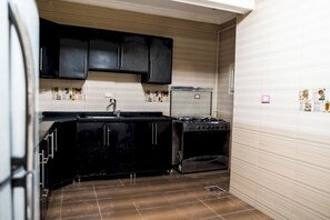 A compact kitchen with black cabinets, a stove, and a refrigerator. - Deluxe Twin Room with Panoramic View (Sheikh Zayed City)