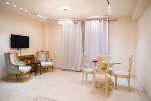 A dining area with a round table and chairs, a television mounted on the wall, and a large window with curtains. - Deluxe Twin Room with Panoramic View (Sheikh Zayed City)