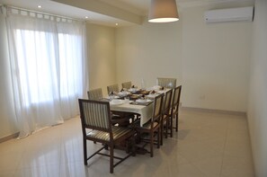 A dining area with a table set for four, surrounded by chairs, in a room with a tiled floor and a ceiling light fixture. - Sky Studio | Cairo Keys New Cairo Residence (New Cairo City)