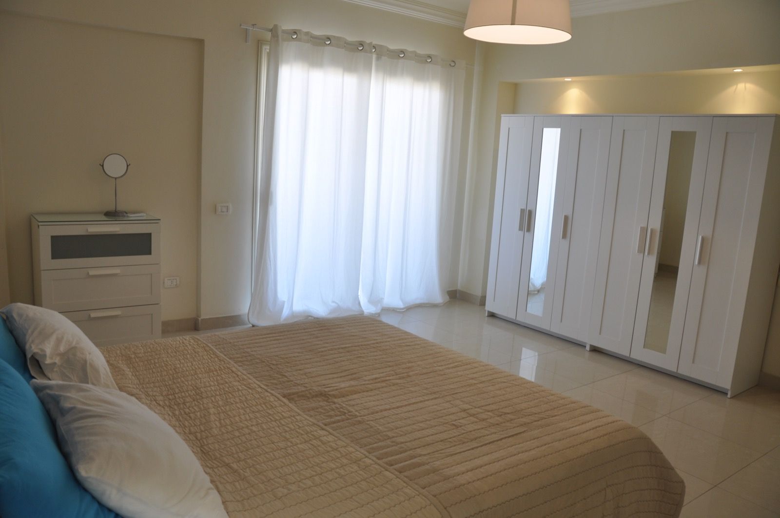 A bedroom with a bed, a wardrobe, a bedside table, and a lamp.