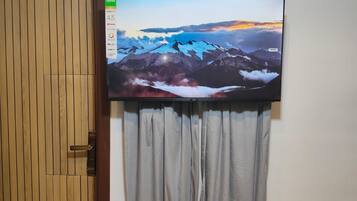A flat-screen TV mounted on a wall above a grey curtain, with a wooden door to the left.